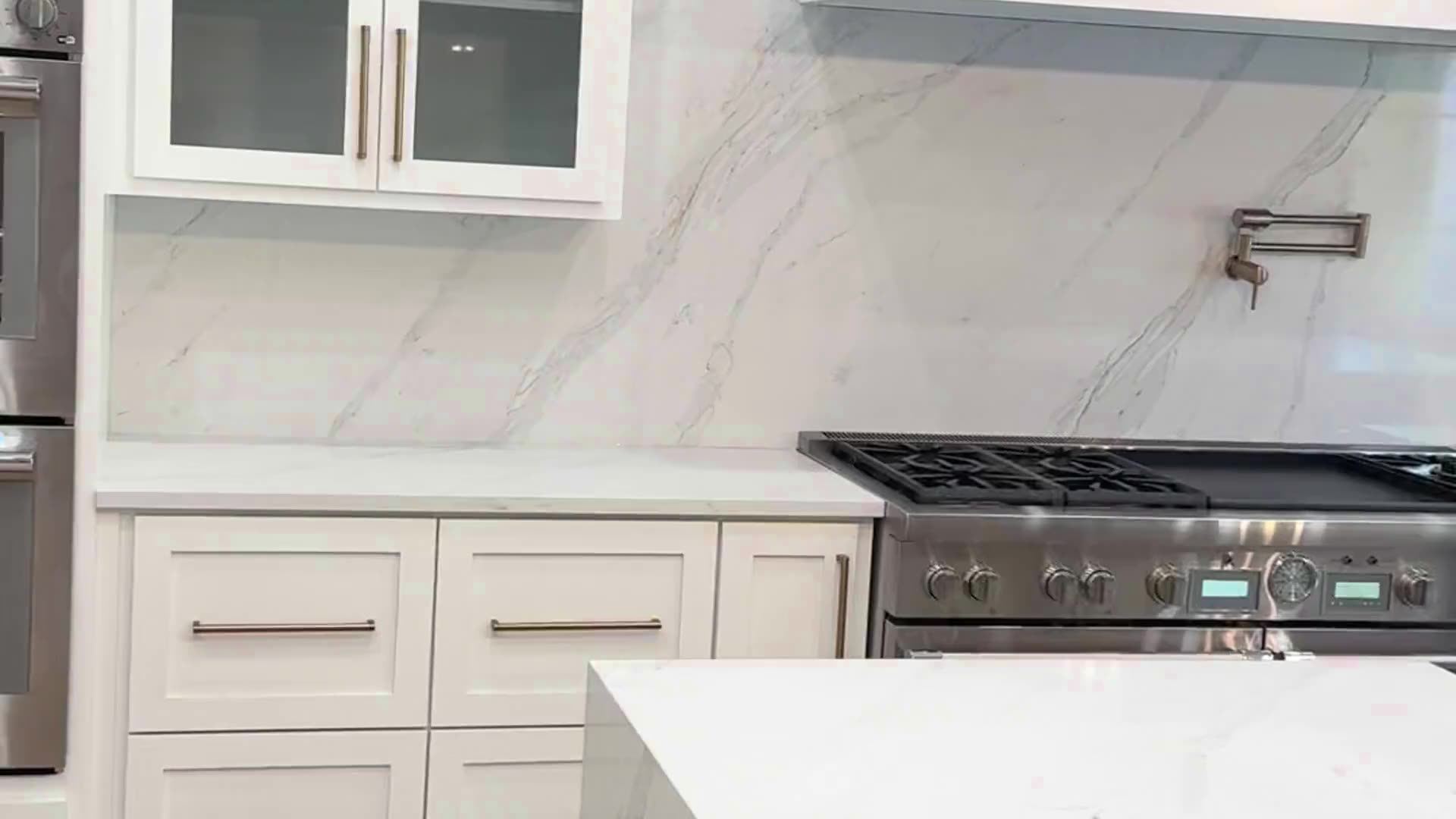 White marble backsplash behind a stainless range, with a white stone island counter in front