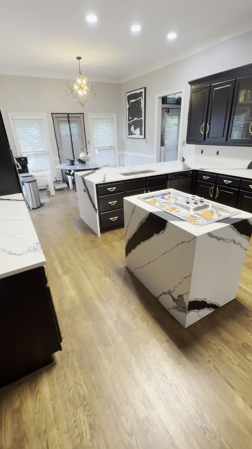Black and white veined waterfall island in a kitchen with black cabinets and brass hardware