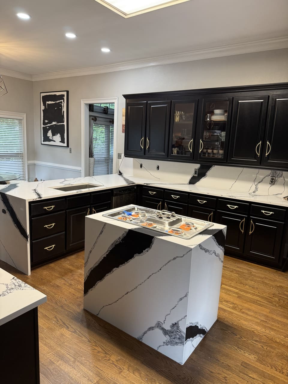 Kitchen island with a white and black veined waterfall countertop in front of dark cabinets with brass pulls