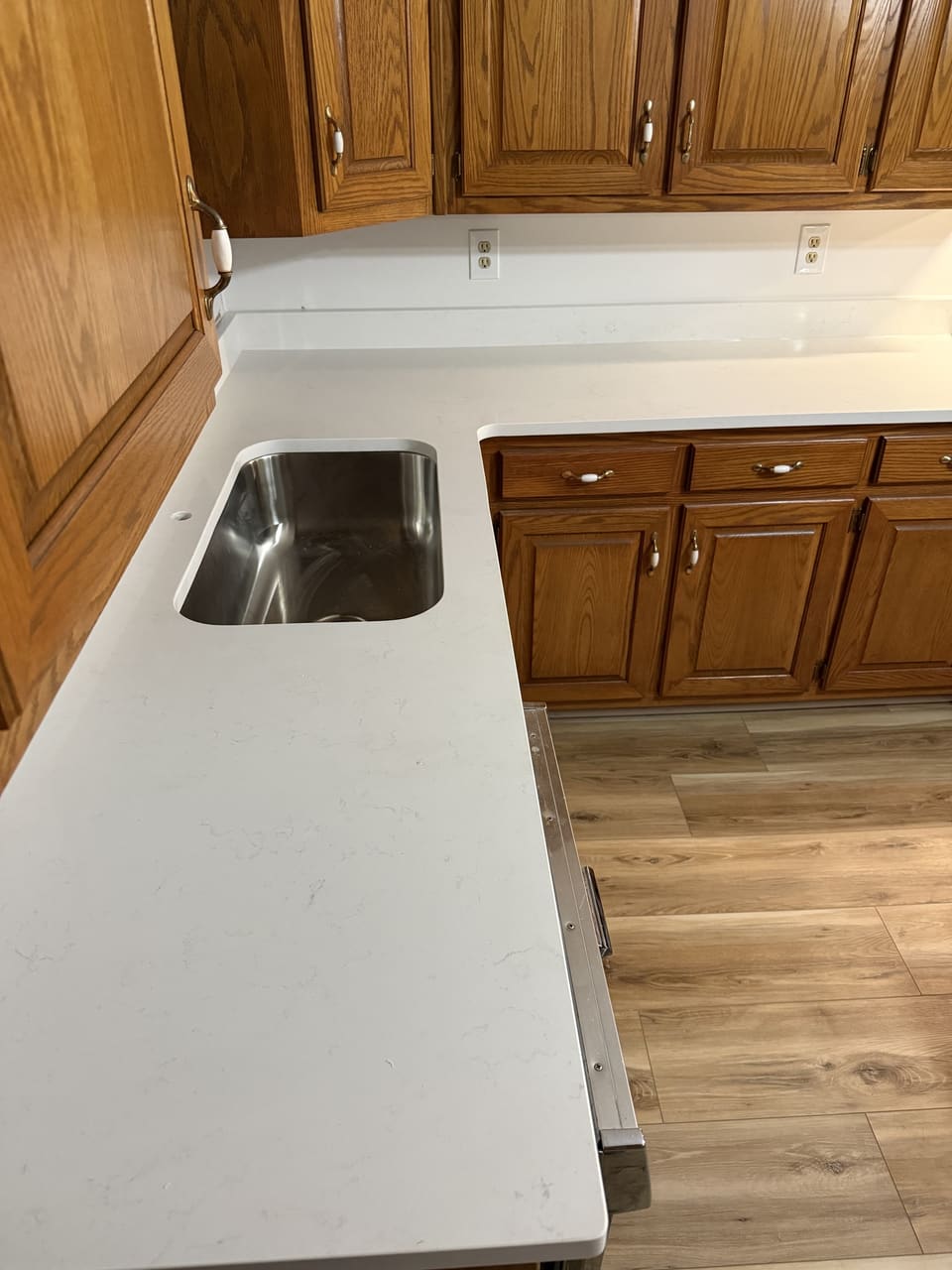 L shaped white countertop with an undermount stainless sink under oak cabinets