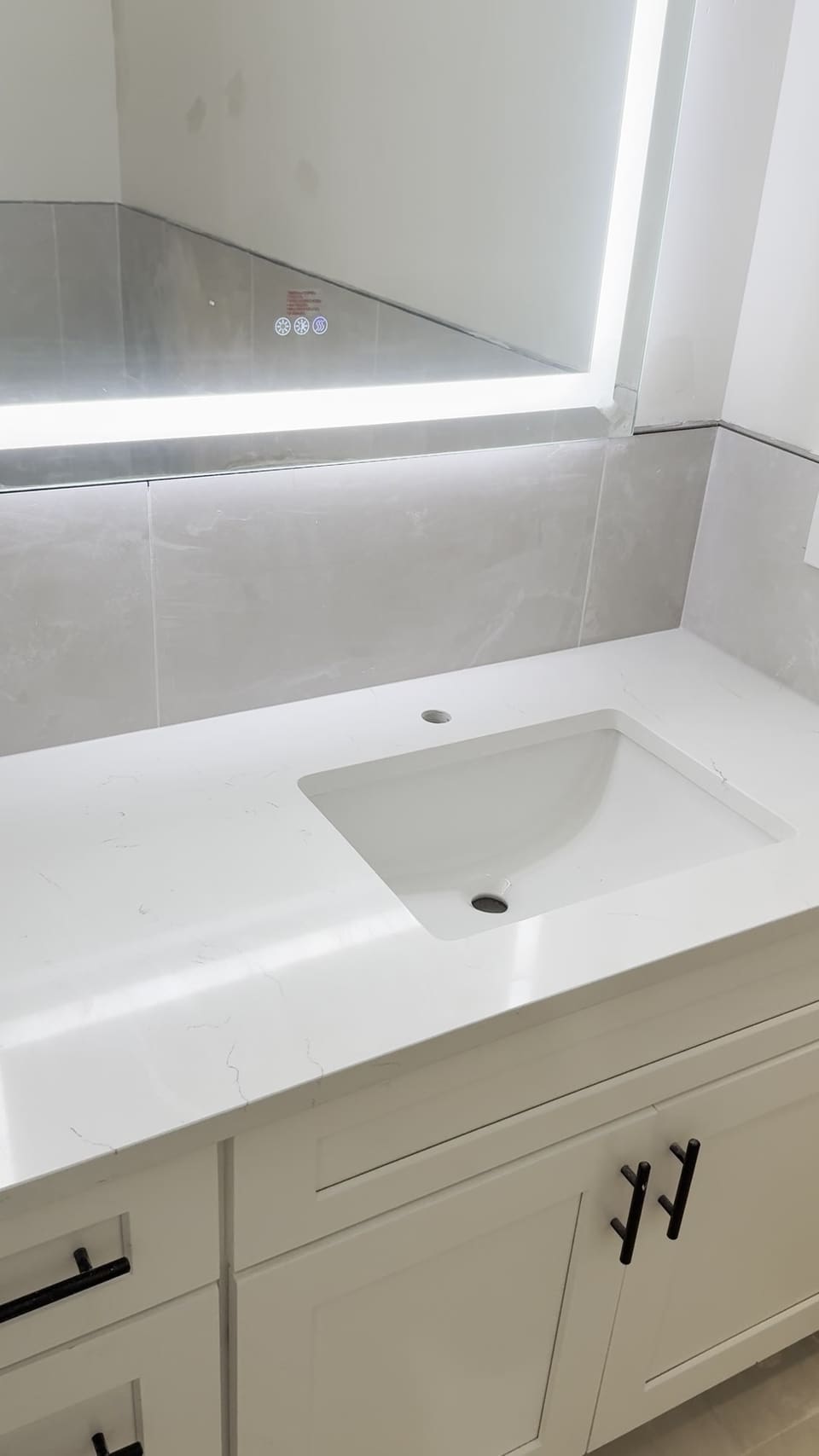 White veined vanity top with an undermount sink under a backlit mirror