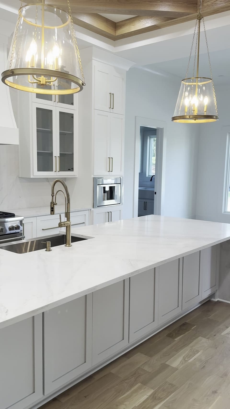 Long white stone kitchen island with a brass faucet under glass pendant lights