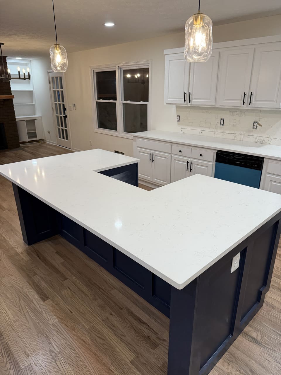 L shaped white countertop island on navy blue cabinets under glass pendant lights