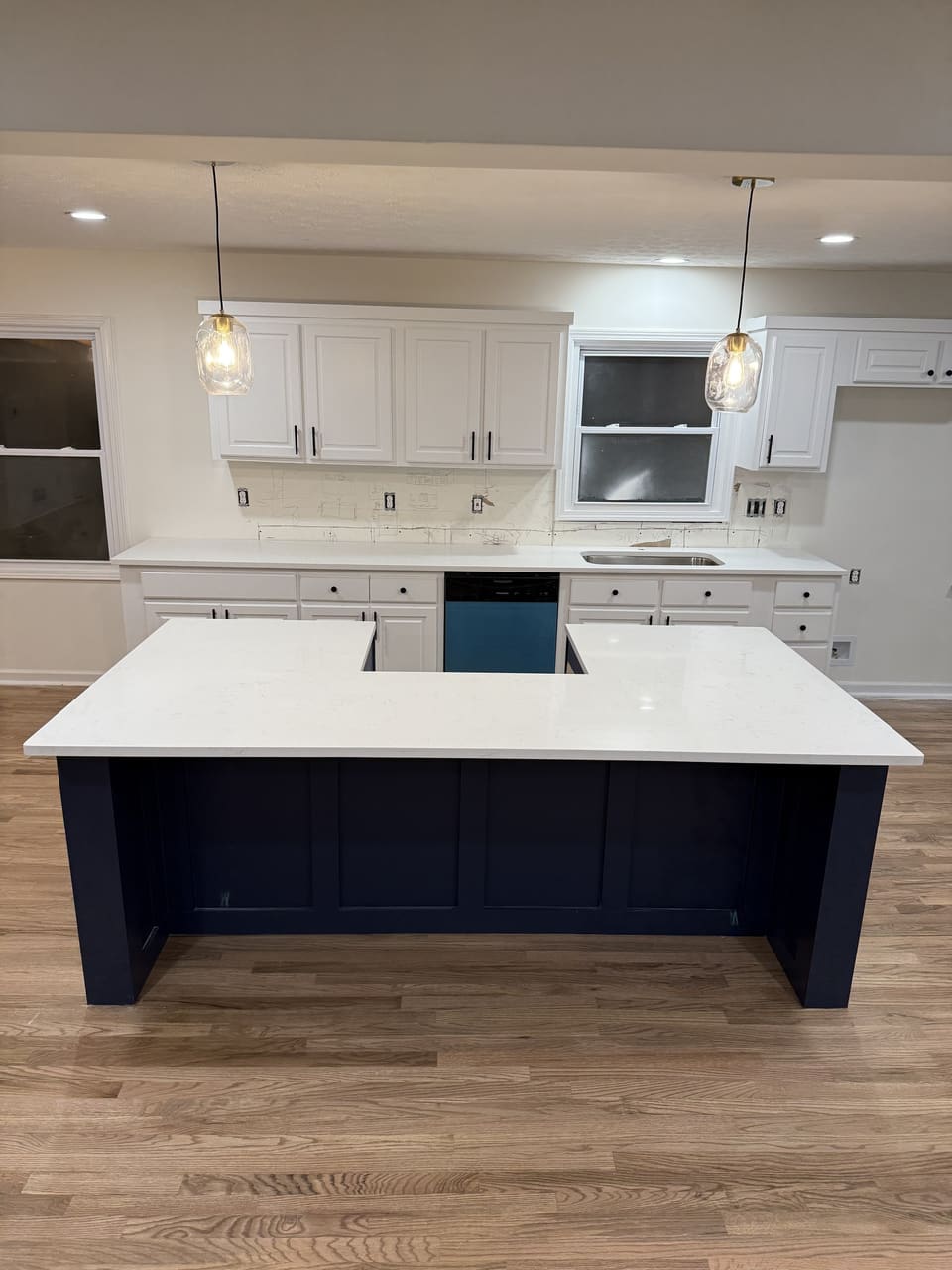 Large white countertop island on navy cabinets with matching white perimeter counters and pendant lights