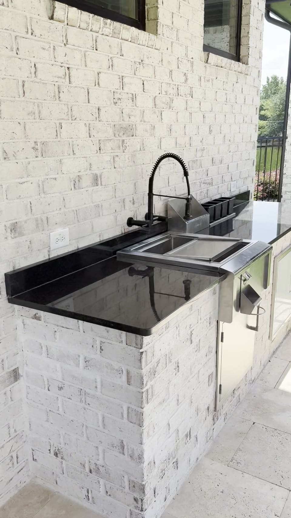 Black stone outdoor kitchen counter with a sink and grill set into white painted brick