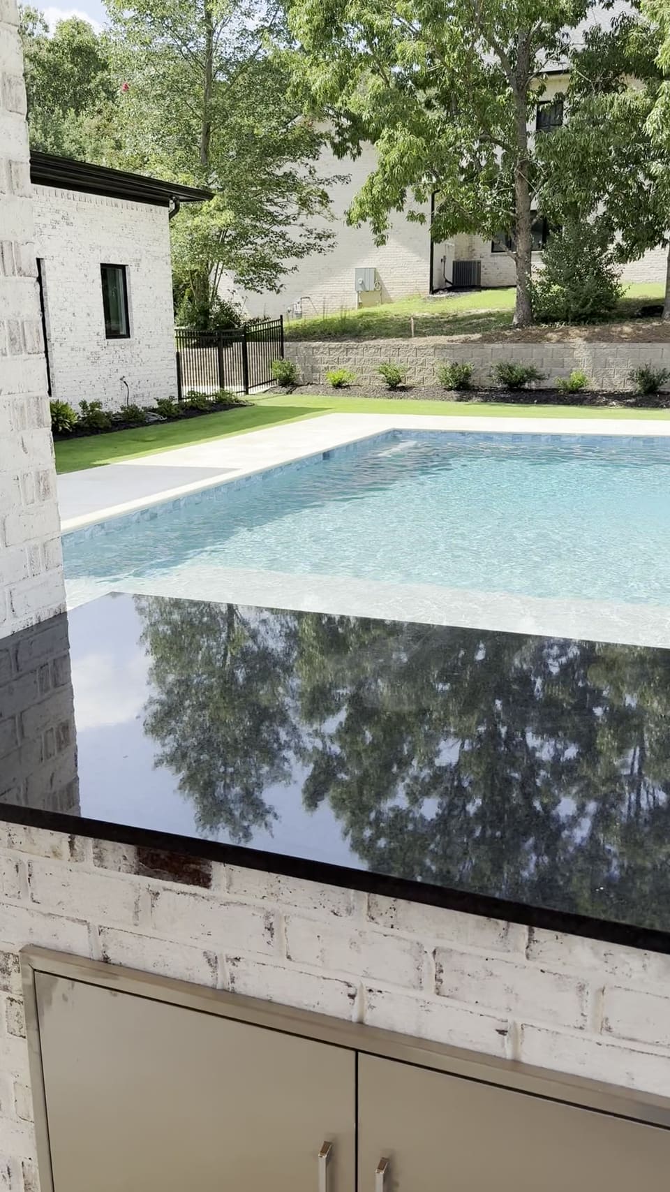 Polished black stone outdoor countertop reflecting the trees beside a backyard pool