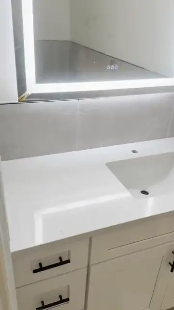 White vanity top under a backlit mirror