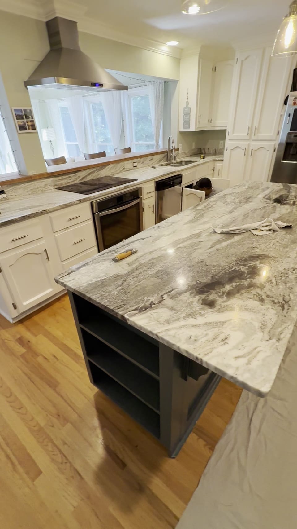 Gray and white veined stone island with open shelving under it in a white kitchen